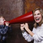 Young boy speaking into megaphone, woman holding megaphone to her ear